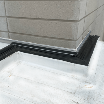 Flat roof expansion joint transition to corner of a wall and roof intersection